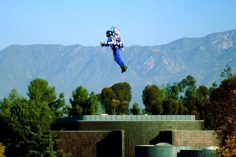 The Rocketman flying over rooftops with mountains in the background